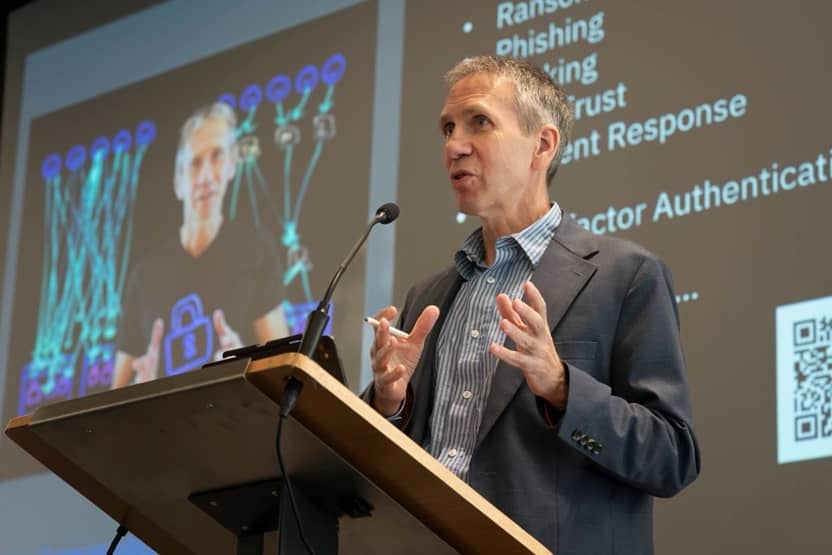 Jeff Crume speaking at a lectern during the Duke Cybersecurity Conference, a slide listing ransomware, phishing, zero trust and incident response projected behind him